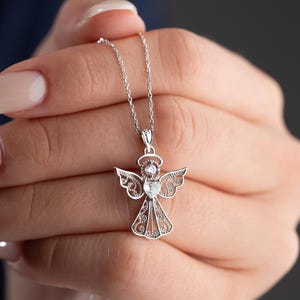 May include: A silver angel pendant necklace. The pendant features an angel design with intricate wing and body details, and a halo. The necklace is on a delicate chain. The angel pendant is approximately 1 inch in height.