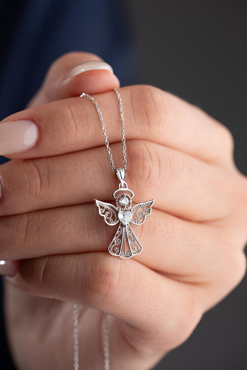 May include: A silver angel pendant necklace. The pendant features an angel design with intricate wing and body details, and a halo. The necklace is on a delicate chain. The angel pendant is approximately 1 inch in height.