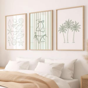 May include: Three framed art prints with a beach theme. One print features various seashells and starfish, another a bikini with the text "meet us at the beach", and the third, three palm trees. The frames are light wood.