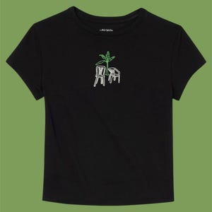 Puede incluir: Camiseta negra con un diseño bordado en verde de una palmera y dos sillas.
