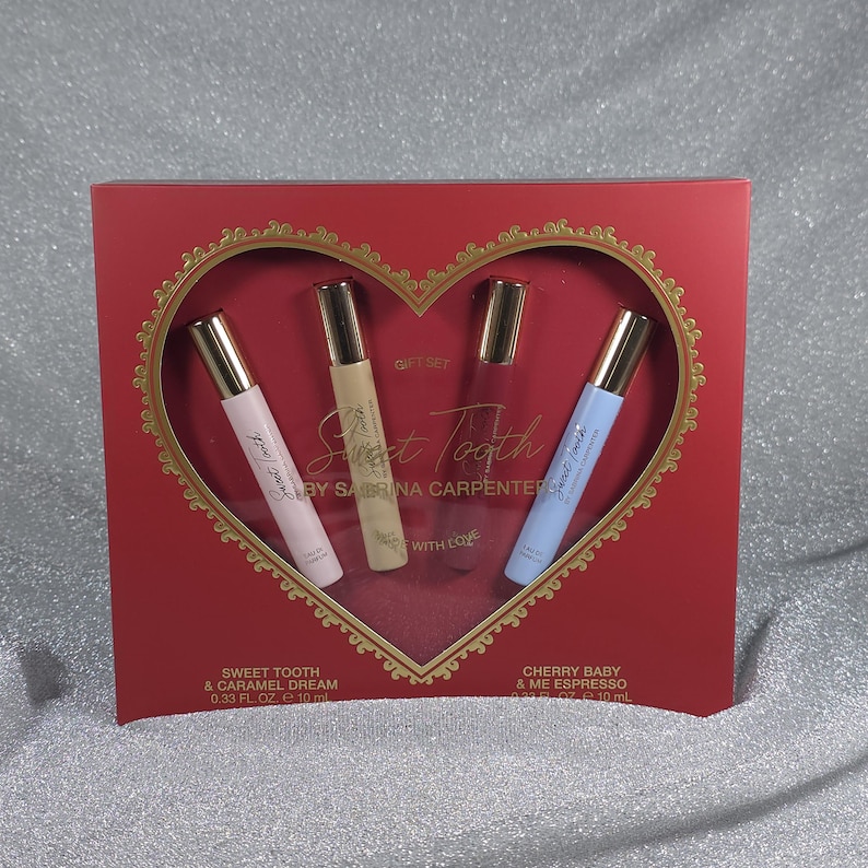 May include: A red gift set featuring four perfume bottles. The set is shaped like a heart with gold trim. The bottles are pink, beige, and blue, with gold caps. The text "Sweet Tooth" and "Cherry Baby" are visible on the bottles.