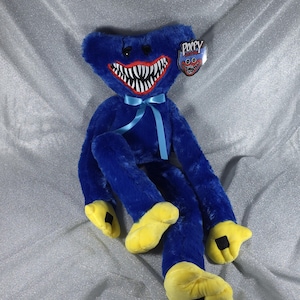 May include: A blue plush toy with long limbs, yellow hands and feet, and a wide mouth featuring sharp white teeth. A light blue ribbon is tied around its neck. A tag attached to the head displays the text Poppy Playtime with a character graphic.