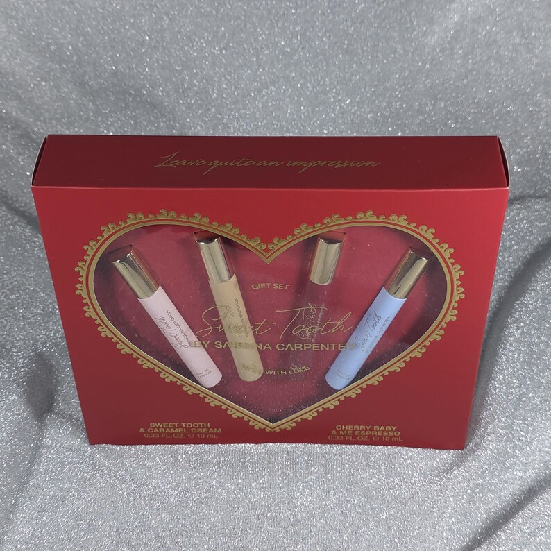 May include: A red gift set box with a heart-shaped window displaying three perfume bottles. The bottles are pink, beige, and blue, with gold caps. The box reads "Sweet Tooth" and "Leave quite an impression."