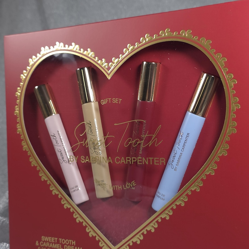 May include: A red gift set featuring four perfume bottles in a heart-shaped window. The bottles are in pink, beige, red, and light blue, with gold caps. The text "Sweet Tooth by Sabrina Carpenter" is printed on the bottles.