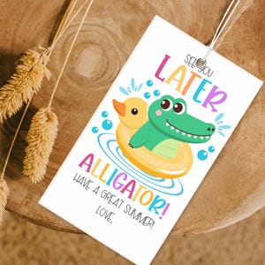 Puede incluir: Una tarjeta blanca con un cocodrilo verde que lleva un flotador inflable amarillo con un pato de goma amarillo dentro. La tarjeta dice "See you later alligator! Have a great summer! Love."
