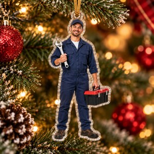 May include: A flat, die-cut acrylic Christmas ornament featuring a smiling mechanic wearing a navy blue jumpsuit and a matching cap. The mechanic holds a large silver adjustable wrench in one hand and a black and red plastic toolbox in the other.