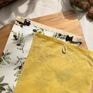 May include: Two rectangular storage bags. One bag features a cream background with a green olive branch pattern and two black plastic side-release buckles. The second bag is solid yellow with a small white cord loop attached to the top edge.