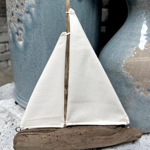May include: A small decorative sailboat with a white sail and a driftwood hull. The sail is attached to a wooden mast. The boat is a nautical-themed item, perfect for home decor.