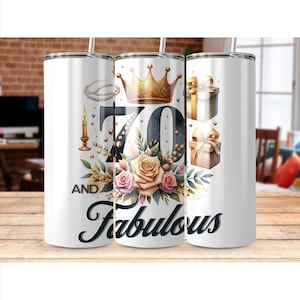 Op de afbeelding: Witte geïsoleerde tumbler met een bloemen- en kroonontwerp. De tumbler heeft de tekst "70 and Fabulous" met een gouden kroon, roze en crèmerozen en geschenkdozen. Een parelketting en kaars zijn ook inbegrepen.
