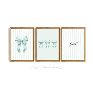 以下が含まれることがあります： 3つの額入りアートプリントのセット。 金色のフレームには、水彩画のリボン、複数のリボン、そして「Sweet」という文字が描かれています。 背景は、水色の縦縞模様です。