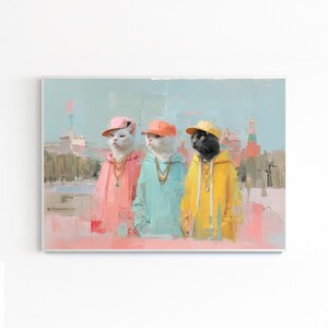 以下が含まれることがあります： フード付きスウェットと野球帽をかぶった3匹の猫が描かれた、額入りのアートプリント。 猫はピンク、青、黄色で描かれ、金のチェーンネックレスをしています。 背景には、薄い青い空とピンクと白の建物がある都市景観が描かれています。