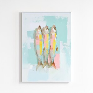 以下が含まれることがあります： ピンク、黄色、青のアクセントが施された3匹の魚の抽象画。魚は、水色とピンクの筆致を背景に垂直に配置されています。アートワークは白いフレームで囲まれています。