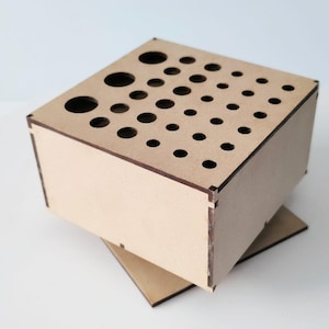 Peut inclure: Un organisateur en bois brun clair avec de nombreux trous circulaires de différentes tailles sur le dessus. La boîte, avec des joints visibles, repose sur une base assortie. Idéal pour ranger de petits objets.