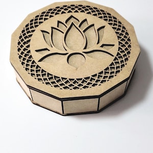 Peut inclure: Boîte en bois octogonale découpée au laser. Le couvercle présente un motif de fleur de lotus détaillé au centre, entouré d'un motif en treillis complexe. La boîte est en bois brun clair.