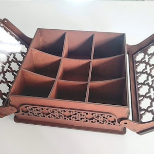 Peut inclure: Boîte en bois marron avec couvercle à charnière et neuf compartiments. Les portes présentent des motifs découpés décoratifs. Les portes sont ouvertes, révélant l'intérieur. La boîte est conçue pour le rangement.
