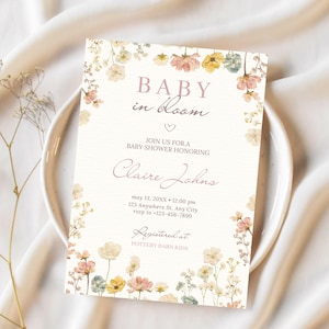 May include: A baby shower invitation with floral accents. The invitation features the text "BABY in bloom" and details for the event, including the name "Claire Johns", date, time, and RSVP information. The invitation is decorated with pastel-colored flowers.