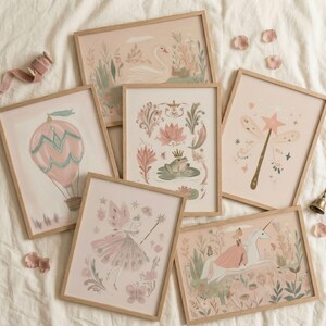 Puede incluir: Una colecci&oacute;n de l&aacute;minas art&iacute;sticas enmarcadas con tem&aacute;tica de cuento de hadas. Las l&aacute;minas presentan ilustraciones de un cisne, un globo aerost&aacute;tico, un hada, una rana, una varita m&aacute;gica y un unicornio. La paleta de colores incluye rosas suaves, verdes y tonos beige, con marcos de madera.