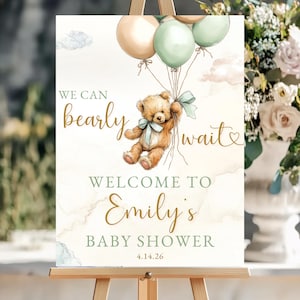 Peut inclure: Panneau de bienvenue pour une baby shower sur un chevalet. Le panneau présente un ours en peluche tenant des ballons, avec le texte "We can bearly wait" et "Welcome to Emily's Baby Shower" en or et vert. La date 4.14.26 est également incluse.