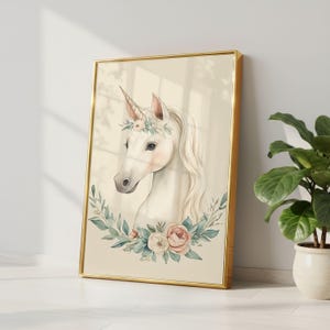 Puede incluir: Una impresi&oacute;n en acuarela enmarcada de un unicornio. El unicornio tiene un pelaje blanco, un cuerno dorado y una corona floral. La obra de arte est&aacute; enmarcada en un marco dorado y presenta una corona de flores y vegetaci&oacute;n alrededor del cuello del unicornio.