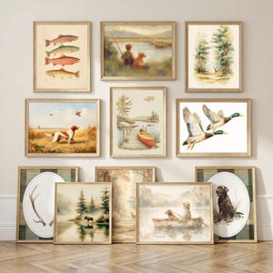 May include: A collection of ten framed wall art prints featuring outdoor themes including fish, a person fishing with a dog, a deer in a forest, a hunting dog in a field, a red canoe at a dock, flying ducks, an antler, a moose, and a dog in a boat.