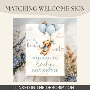 May include: A baby shower welcome sign featuring a watercolor illustration of a teddy bear holding blue balloons. The sign reads "We can bearly wait" and welcomes guests to Emily's baby shower on April 14, 2026. The sign is linked in the description.