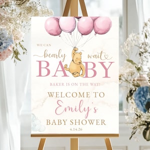 May include: A baby shower welcome sign on an easel. The sign features pink balloons, a Winnie the Pooh illustration, and the text "Bearly Wait Baby" and "Welcome to Emily's Baby Shower". The date 4.14.26 is also included.