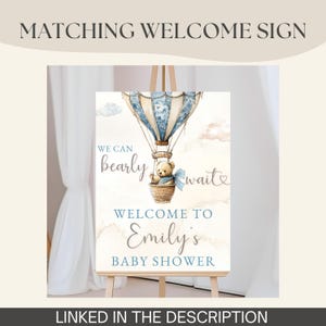 May include: A welcome sign for a baby shower, featuring a watercolor illustration of a hot air balloon with a teddy bear in a basket. The sign includes the text "We can bearly wait" and "Welcome to Emily's Baby Shower."