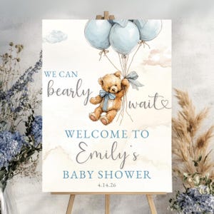 May include: A baby shower sign with a watercolour illustration of a teddy bear floating with blue balloons. The sign says "We can bearly wait" and welcomes guests to Emily's baby shower, with the date 4.14.26.