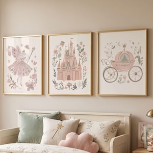 May include: Three framed wall art prints in gold frames featuring illustrations in soft pink and muted green tones. The left print shows a fairy with a wand, the center print depicts a castle, and the right print displays a pumpkin carriage.