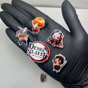 May include: A selection of anime stickers featuring characters from "Demon Slayer." The stickers depict various characters and the series logo. The stickers are colourful and have a glossy finish.