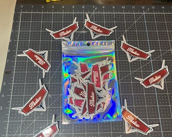 Puede incluir: Primer plano de una bolsa de plástico transparente llena de pegatinas rojas y blancas. Las pegatinas tienen todas el mismo diseño y muestran la palabra "Mateo" en blanco sobre fondo rojo. Las pegatinas están dispuestas de forma aleatoria dentro de la bolsa.