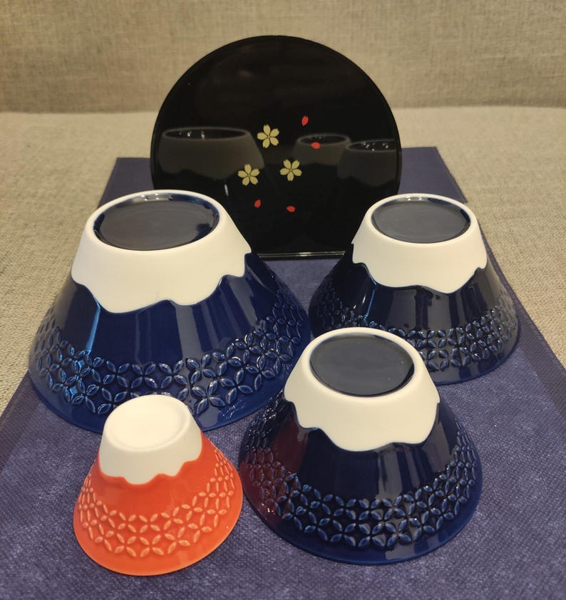 Pu&ograve; includere: Set di quattro ciotole in ceramica blu e bianca con un design a forma di montagna. Le ciotole sono annidate l'una dentro l'altra e sono decorate con un cappello di neve bianco e un design di montagna blu. La ciotola pi&ugrave; piccola &egrave; rossa.