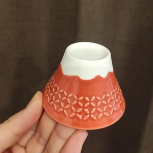 Pu&ograve; includere: Una piccola ciotola di ceramica rossa con un bordo bianco e un motivo floreale. La ciotola ha la forma di una montagna.