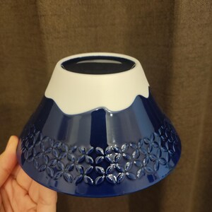 Pu&ograve; includere: Una ciotola in ceramica blu e bianca a forma di Monte Fuji. La ciotola ha un bordo bianco e una base blu con un motivo di piccoli fiori bianchi.