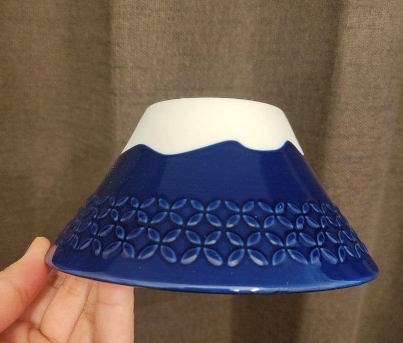 Pu&ograve; includere: Una ciotola in ceramica blu e bianca con un design a forma di montagna e un bordo bianco. La ciotola ha un motivo di piccoli fiori blu sul fondo.
