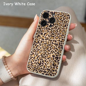 May include: Ivory white phone case with a leopard print pattern. The case has a protective bumper and features the text "Ivory White Case" at the top. The case is held in a person's hand.
