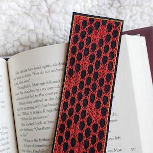May include: A black bookmark with a red embroidered pattern. The bookmark has a gold border.
