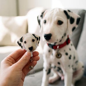以下が含まれることがあります： 白い背景に黒い斑点のあるダルメシアンの子犬の顔がプリントされた透明なアクリル製バッジリール。伸縮自在のコードと、衣服やアクセサリーに取り付けるための金属製クリップが付いています。