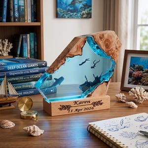 May include: A custom wooden and blue resin desk ornament featuring an underwater scene with a whale shark, two scuba divers, and a shipwreck. The rectangular wooden base is engraved with the name Karen and the date 11 Apr 2026 with leaf accents.