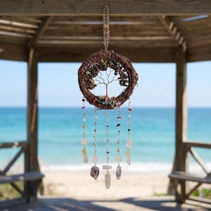 May include: A circular wall hanging featuring a brown woven vine wreath frame containing a copper wire tree sculpture with small gemstone leaves. Five dangling strands of silver chain are adorned with various colorful crystal beads and stones.