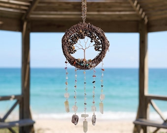 May include: A circular wall hanging featuring a brown woven vine wreath frame containing a copper wire tree sculpture with small gemstone leaves. Five dangling strands of silver chain are adorned with various colorful crystal beads and stones.