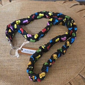 May include: A black fabric dog leash featuring a colorful pattern of heart-shaped candies and paw prints. The leash has a gathered, elasticized design and includes a silver metal swivel snap hook and a brown paper tag labeled Threads & Things Co.