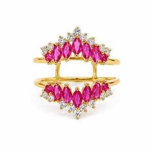 Könnte beinhalten: Ein goldener Doppelring mit zwei symmetrischen Reihen aus leuchtend pinkfarbenen Steinen im Marquise-Schliff und runden, klaren weißen Steinen. Das Design besteht aus zwei verbundenen Bändern mit einer kronenartigen Anordnung der Edelsteine.