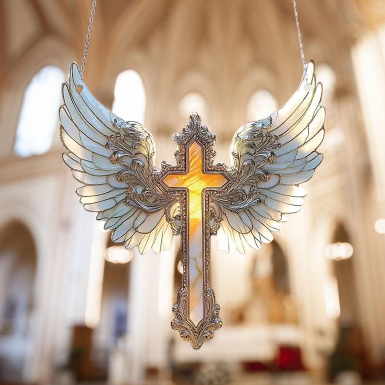 May include: A decorative cross with angel wings, featuring a silver frame and iridescent accents. The cross has a yellow center and is suspended by a chain. The wings are white with silver detailing, creating a religious-themed ornament.