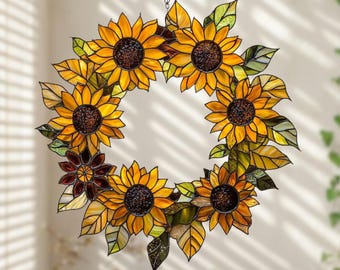 May include: A stained glass sunflower wreath with yellow, orange, and brown petals and green leaves. The wreath is hanging from a chain and is a decorative item.