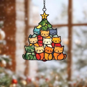 May include: A stained glass Christmas tree ornament featuring a design of smiling cats in various colors. The tree is topped with a yellow star and hangs from a black chain. The cats are arranged in a tree shape.
