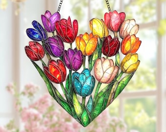 May include: A heart-shaped stained glass window hanging featuring a bouquet of colorful tulips. The tulips are in shades of red, orange, yellow, purple, and blue, with green leaves. The window is suspended by a black chain.