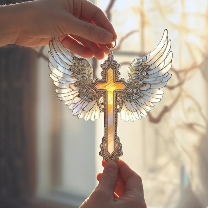 May include: A decorative cross with angel wings, held up to the light. The cross is gold-colored with a yellow center, and the wings are white and silver. The design is ornate and detailed, suitable for home decor.