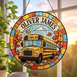 May include: A round, stained-glass window hanging with the name "OLIVER JAMES" at the top. A yellow school bus is in the center, with "SCHOOL BUS" above it. The design includes autumn leaves and a blue sky background.