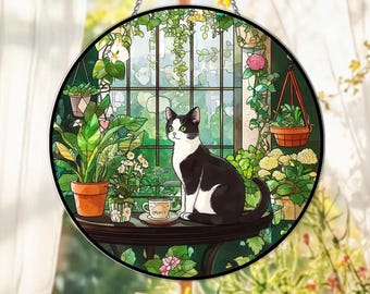 May include: Round stained glass window art featuring a black and white cat with green eyes, sitting on a table with a teacup. The background shows a sunlit indoor garden with potted plants and a window.
